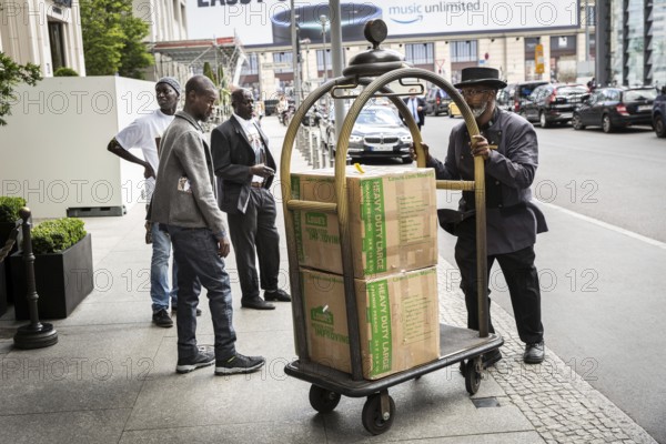 DEU Germany Germany Berlin Supporters of the Senegalese president in front of the Ritz Carlton Hotel at Potsdamer Platz. A doorman pushes a hotel trolley under the watchful eye of three Senegalese