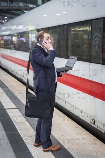 DEU Germany Germany Berlin A passenger stands in front of an ICE train at Berlin Central Station with a laptop on his phone