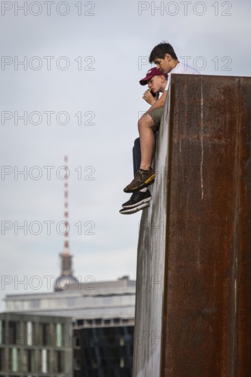 DEU Germany Germany Berlin In summer temperatures, two young people sit on a wall on the Spreebogen and enjoy the view