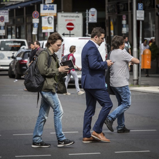 DEU Germany Germany Berlin A young man walks along Friedrichsstrasse reading while another looks at his smartphone