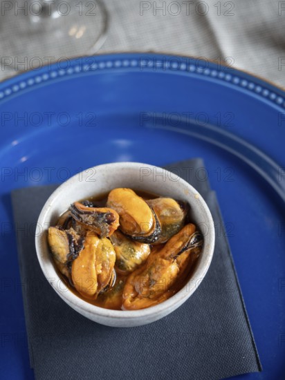 Marinated mussels served as a savory tapa on a rustic white bowl with a blue plate