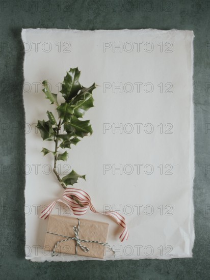 Wrapped present, holly branch, and striped ribbon on textured paper with copy space