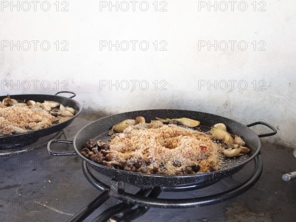 Paella ingredients cooking in pans on gas burners, preparing a spanish meal