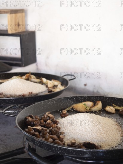 Paella ingredients cooking in a pan, featuring rice, mushrooms, and garlic