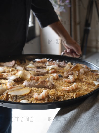 Chef carrying a freshly cooked paella with rice, seafood, and meat for serving