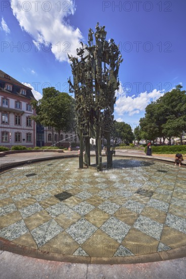 Shrove Tuesday fountain, fountain with bronze sculptures, sculptor Blasius Spreng, architect Helmut Gräf, general architecture, houses, pedestrians and seated people as secondary motifs, trees, blue sky, cumulus clouds, Schillerplatz square, Mainz, state capital, district-free city, Rhineland-Palatinate, Germany