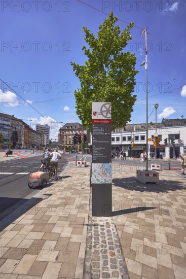 Stele with location sign, traffic area, street, square, sidewalk made of concrete paving stones, general architecture, cyclists and pedestrians as a secondary motif, tree, intersection of Schillerstraße with Große Bleiche and Münsterplatz, Mainz, state capital, district-free city, Rhineland-Palatinate, Germany