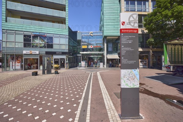 Stele with location sign, Roman passage, shopping center, general architecture, modern building, commercial building, shop, retail, sidewalk made of concrete paving stones and paving stones with pattern, pedestrian zone, trees, blue sky, cloudless, intersection of Cardinal-Volk-Platz with Emmeransstraße, Pfandhausstraße and Stadthausstraße, Mainz, state capital, district-free city, Rhineland-Palatinate, Germany
