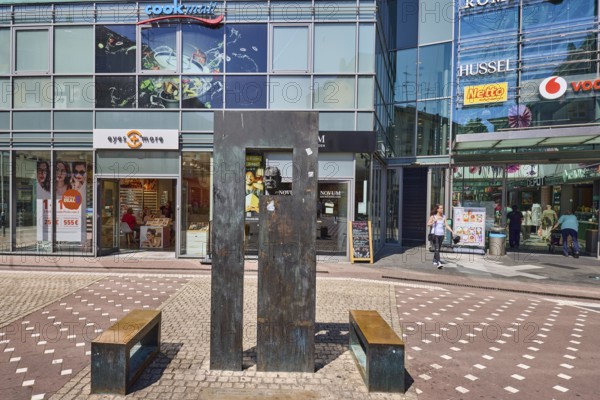 Stele with bust of Cardinal Hermann Volk, sculptor Karlheinz Oswald, pedestrian zone, commercial building, shops, retail stores, glass façade, shop window, sidewalk made of concrete paving stones and paving stones with pattern, sunny, Cardinal-Volk-Platz, Mainz, state capital, district-free city, Rhineland-Palatinate, Germany