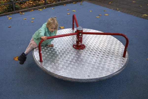 Outdoor shot, little girl, child, 4 years, blonde, playing on carousel, children's playground, slipping off, danger, autumn leaves, autumn, Stuttgart, Baden-Württemberg, Germany