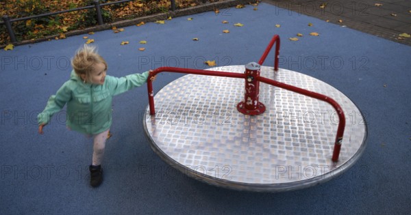 Outdoor shot, little girl, child, 4 years, blonde, playing with carousel, movement effect, children's playground, autumn leaves, autumn, autumn, Stuttgart, Baden-Württemberg, Germany