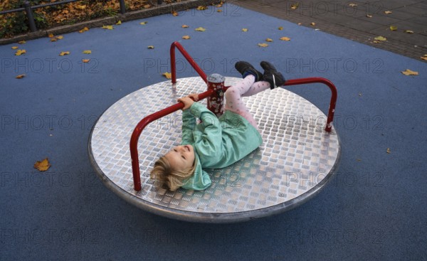 Outdoor shot, little girl, child, 4 years, blonde, playing on carousel, children's playground, autumn leaves, autumn, Stuttgart, Baden-Württemberg, Germany