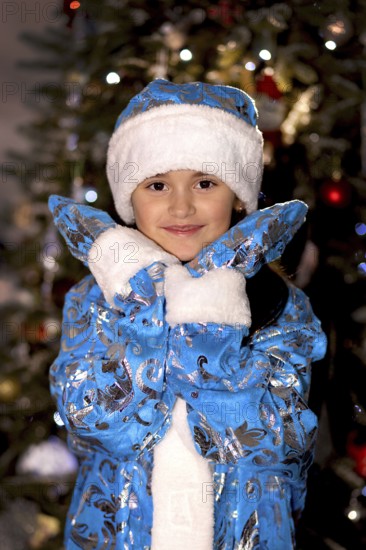 Smiling little girl wearing a blue snegurochka costume in front of a christmas tree.Belarus