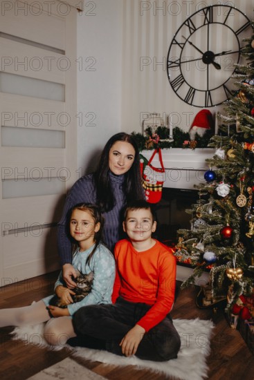 Family group portrait showing a mother, children, and kitten in a festive christmas home setting.Belarus