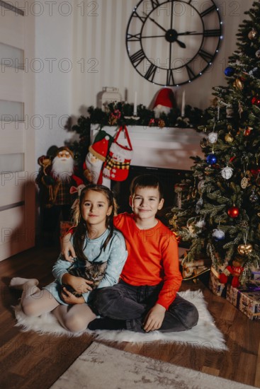 Two cheerful children sitting by a decorated christmas tree enjoying the festive season.Belarus