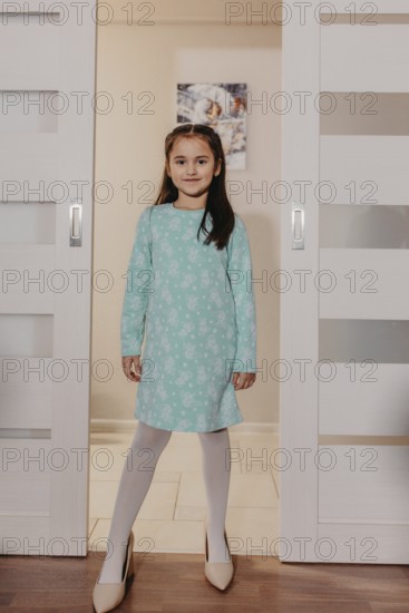 Young girl standing in adult high heels, smiling and playing at home.Belarus