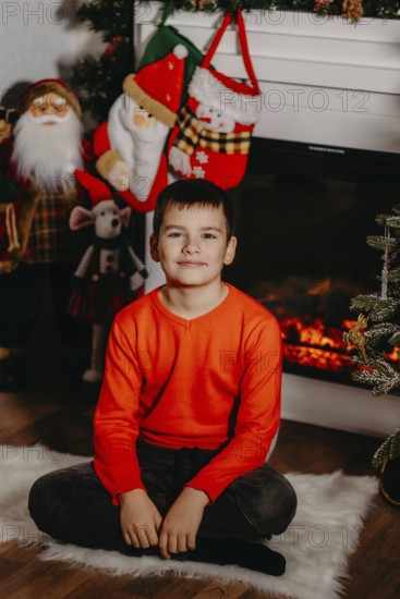 Boy sitting on a white rug in front of a fireplace with christmas decorations.Belarus