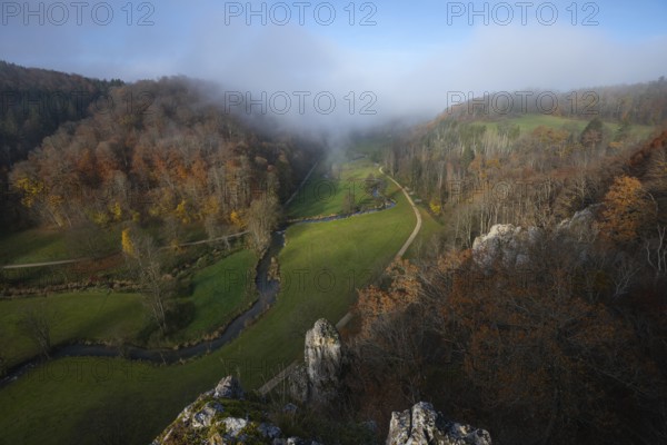Autumn landscape with rising fog over the Grosse Lauter river loop in Lautertal at sunrise. View from above of the picturesque valley with colorful deciduous forest and rolling hills, Großes Lautertal, Baden-Württemberg, Germany