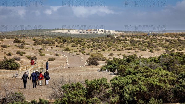 Group of people hiking on a trail through a vast desert landscape towards a complex of buildings, The countryside near Punta Tombo in Argentina