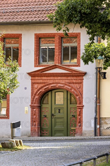 Historic building façade with green door and decorative red stone decorations, surrounded by trees in a peaceful summer scene, historic door in the old town of Arnstadt in Thuringia