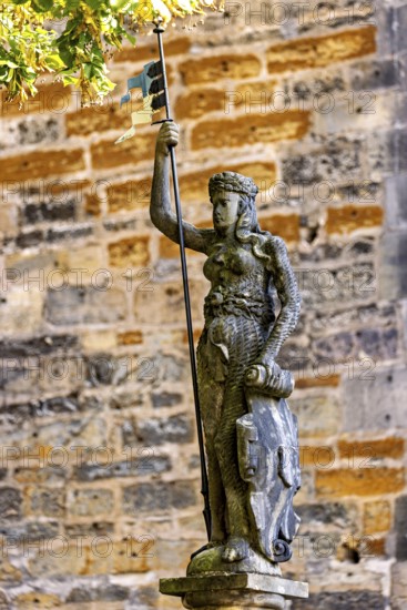 Statue of a figure carrying a flag and a shield in front of an old stone wall, statue and monument in the old town of Arnstadt in Thuringia