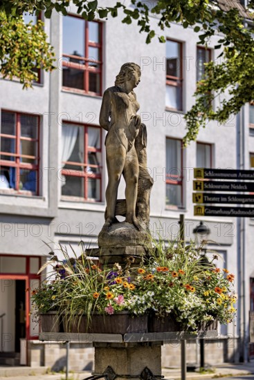 Figure on a fountain with flower frame in front of a building with windows, statue and monument in the old town of Arnstadt in Thuringia