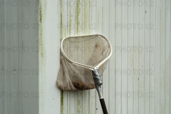 Borken-Hoxfeld, NRW, Germany, A cleaning tool leans against a dirty wall, showing signs of recent use. The metal handle reflects a typical day in a city where maintenance is necessary for cleanliness