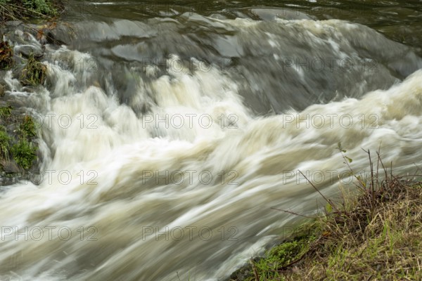 Borken-Hoxfeld, NRW, Germany, Rushing water flows over rocks in a serene natural area, surrounded by lush greenery. Sunlight reflects off the surface, creating a peaceful atmosphere