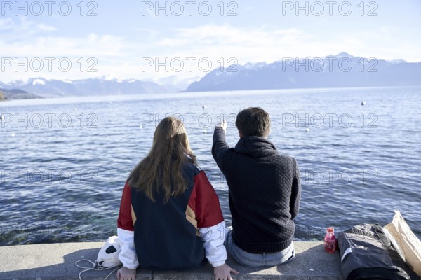 NO MODEL RELEASE, unrecogniseable couple pointing at mountains Les Cornettes de Bise behind Lake Geneva (Genfersee), at lakeside in Lausanna, Kanton Waadt, Switzerland, Europe, daytrip, travel holiday destinations, calm, view of mountainrange