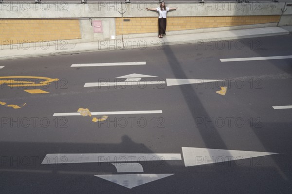 Feeling contrast of light and shadow on the street as metaphor for construction dilemma of warm and hot and cold temperatures in city and traffic design and the used building fundaments sustainability, taking a break, getting a way from it all, feeling inner balance Equilibrium of what one is used to in daily life, conflicted tension, dichotomy, discord, discrepancy, quandary, rifted, mental rift, cleavage, problem, exhaustion, expelled, outcast, exhausted, arms outstretched, urban design materials, sunny weather, resting, lonely, in Magdeburg, Saxony-Anhalt, Germany