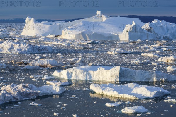 A massive iceberg and iceberg fragments rising from a frozen sea, Ilulissat Icefjord, Greenland