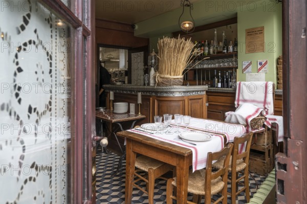 The historic interior of the Auberge Ravoux (Maison de Van Gogh) in Auvers-sur-Oise shows a traditionally set wooden table with chairs and a view of the old counter with bottles, which captures the authentic atmosphere of the period around 1890 and the last whereabouts of the painter Vincent van Gogh, Auvers-sur-Oise, department of Val-d'Oise, Ile-de-France region, France