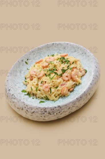 A creamy dish of risoni pasta combined with tender shrimp and fresh herbs is presented in an elegant bowl. This meal showcases simple flavors and a pleasing texture, perfect for a lunch or dinner