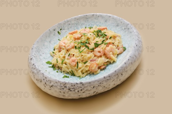 Risoni pasta mixed with tender shrimp is presented on a stylish plate. The dish is topped with fresh herbs, making it an inviting meal perfect for lunch or dinner