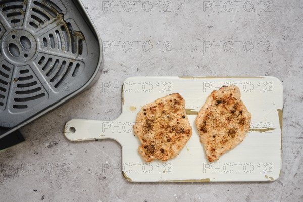 Juicy pork loin cutlets sit on a cutting board after being cooked in an air fryer. These tender pieces are seasoned and ready to enjoy, perfect for a quick and nutritious dinner