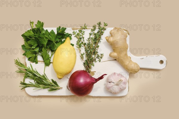 Fresh parsley, lemon, red onion, garlic, ginger, thyme, and rosemary on a chopping board ready for meal preparation