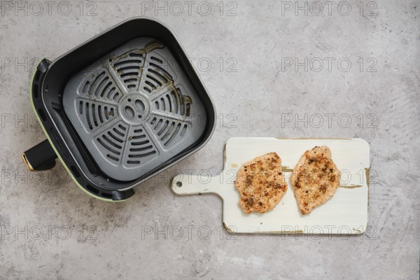 Two perfectly cooked pork sirloin chops rest on a cutting board beside an air fryer basket. The cutlets are seasoned and golden brown, ready to be served as a delicious and easy meal