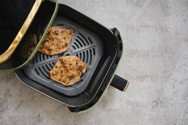 Juicy pork loin cutlets are seasoned and placed inside an air fryer for a healthy cooking method. This image showcases the meal prep taking place in a modern kitchen environment