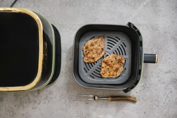 Two cooked seasoned pork sirloin cutlets in the basket of an air fryer. The kitchen setting highlights the convenience of preparing a tasty dish quickly and easily