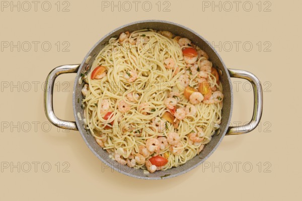 Overhead view of creamy garlic shrimp pasta in a large pan. Plump shrimp and colorful tomatoes mingle with spaghetti, creating a delightful dish ideal for sharing at any meal