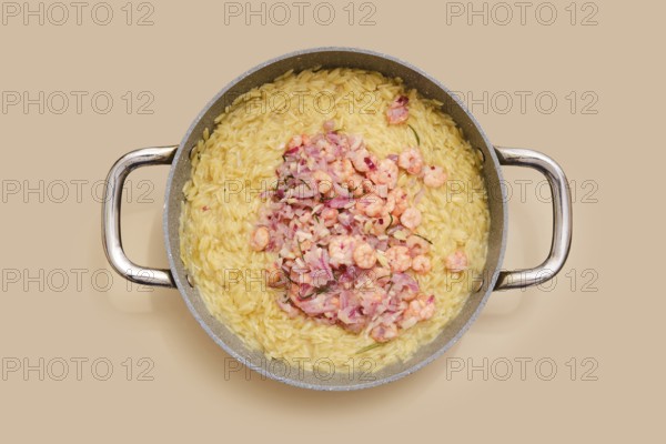 A pot with cooked risoni pasta and fresh shrimps. The dish features a creamy texture and vibrant colours. Ideal for a quick, satisfying meal at home