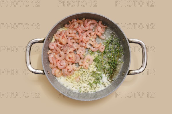 Shrimps and herbs sizzle in a pan, blending with chopped garlic, ginger and olive oil. Process of infusing food with aroma and scents