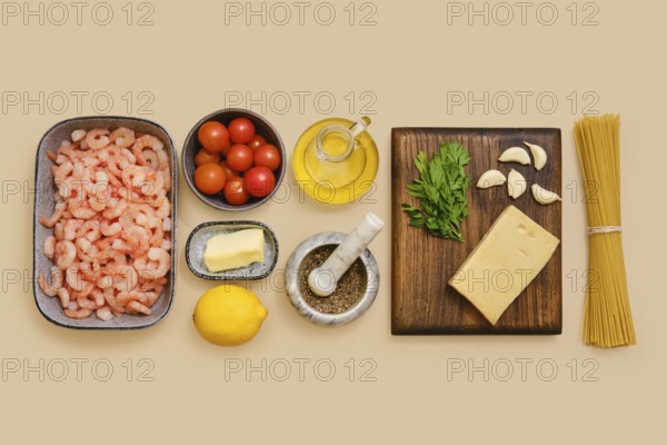 Shrimps, cherry tomatoes, garlic, and parsley lie neatly on a table along with lemon, butter, olive oil, cheese, and pasta