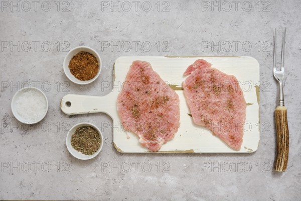 Two pork sirloin chops on a cutting board, seasoned with various spices, in a well-lit kitchen. Ingredients include salt, pepper, and other spices, ready for air frying