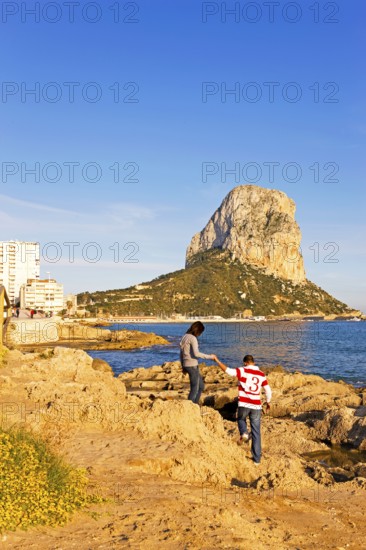Two people on a rocky coast, natural park, in the background rock Penon de Ifach, landmark, Mediterranean Sea, Calpe, Valencia, Costa Blanca, Spain
