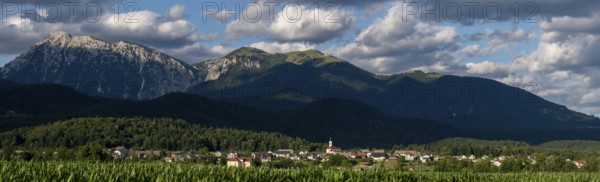 A Slovenian village is nestled between green fields and the imposing peaks of the Julian Alps near Kranj, Slovenia