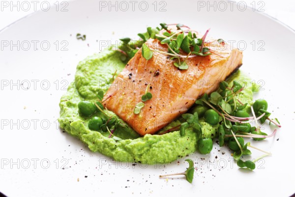 Delicious grilled salmon is placed elegantly on creamy green pea puree. Fresh microgreens and peas add a bright touch, creating an appetizing dish perfect for any meal