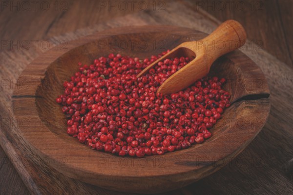 Bright red peppercorns, in a wooden bowl, with a small wooden tray