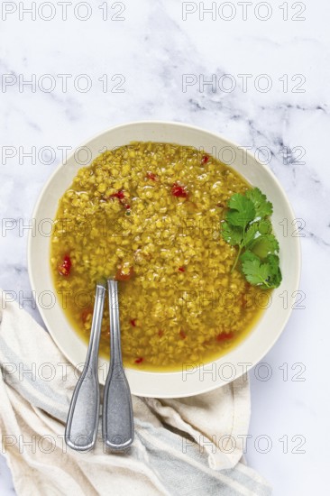 A warm bowl of lentil soup features a golden broth filled with spices and herbs. Fresh cilantro garnishes the dish, adding flavor and color against the marble background