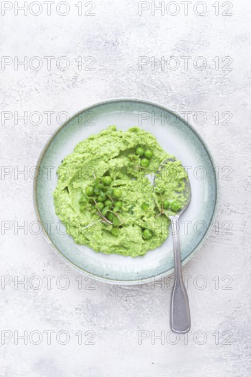 A vibrant green pea puree fills a shallow bowl, topped with fresh peas and microgreens. The dish looks fresh and inviting, ideal for a light, nutritious meal at any time